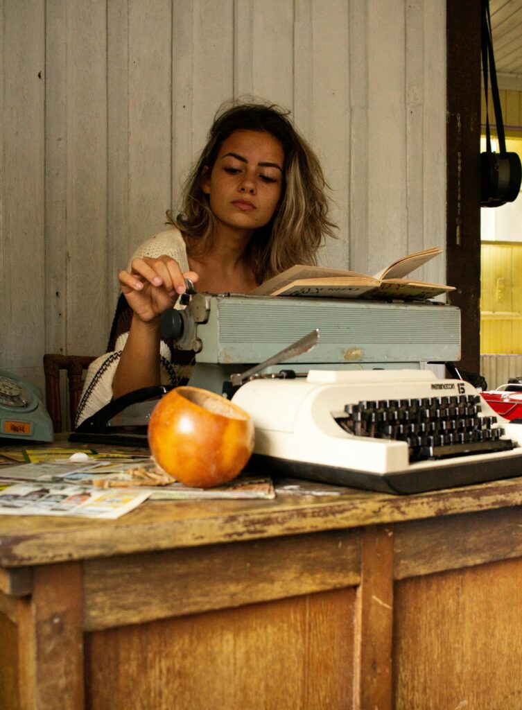 Young woman typing on a vintage typewriter at a rustic wooden desk indoors.