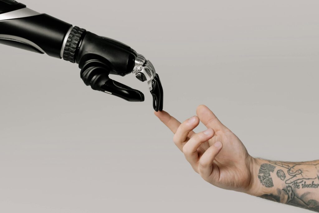 pexels-photo-6153354-6153354 A human hand with tattoos reaching out to a robotic hand on a white background.